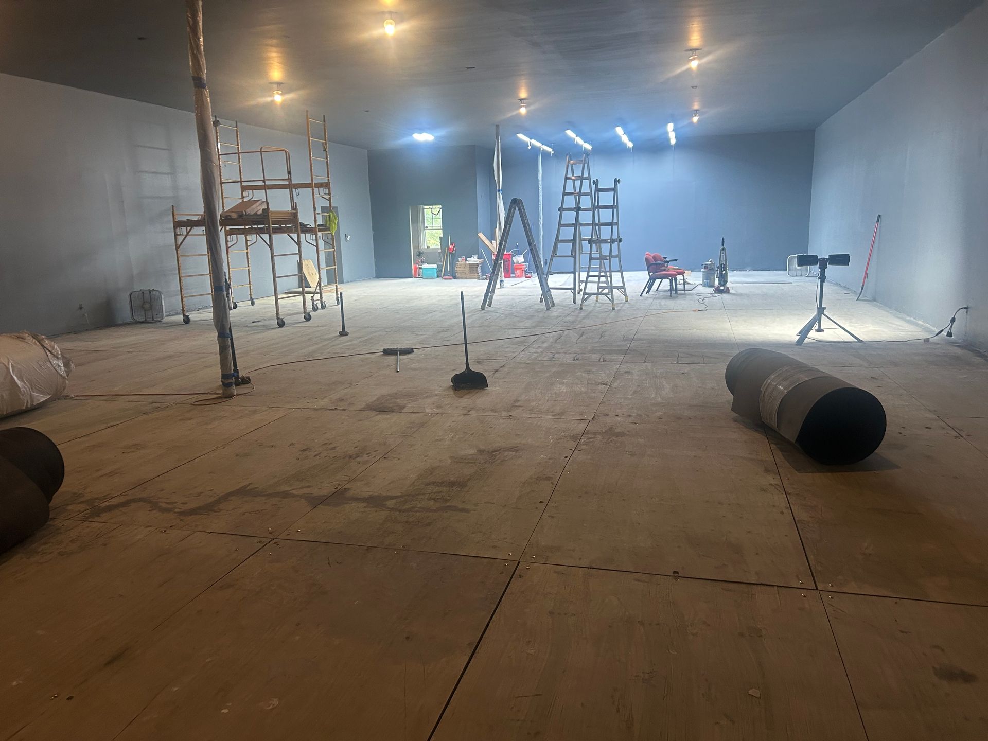 Interior of a large, gray room under construction with construction equipment and debris scattered on the floor.