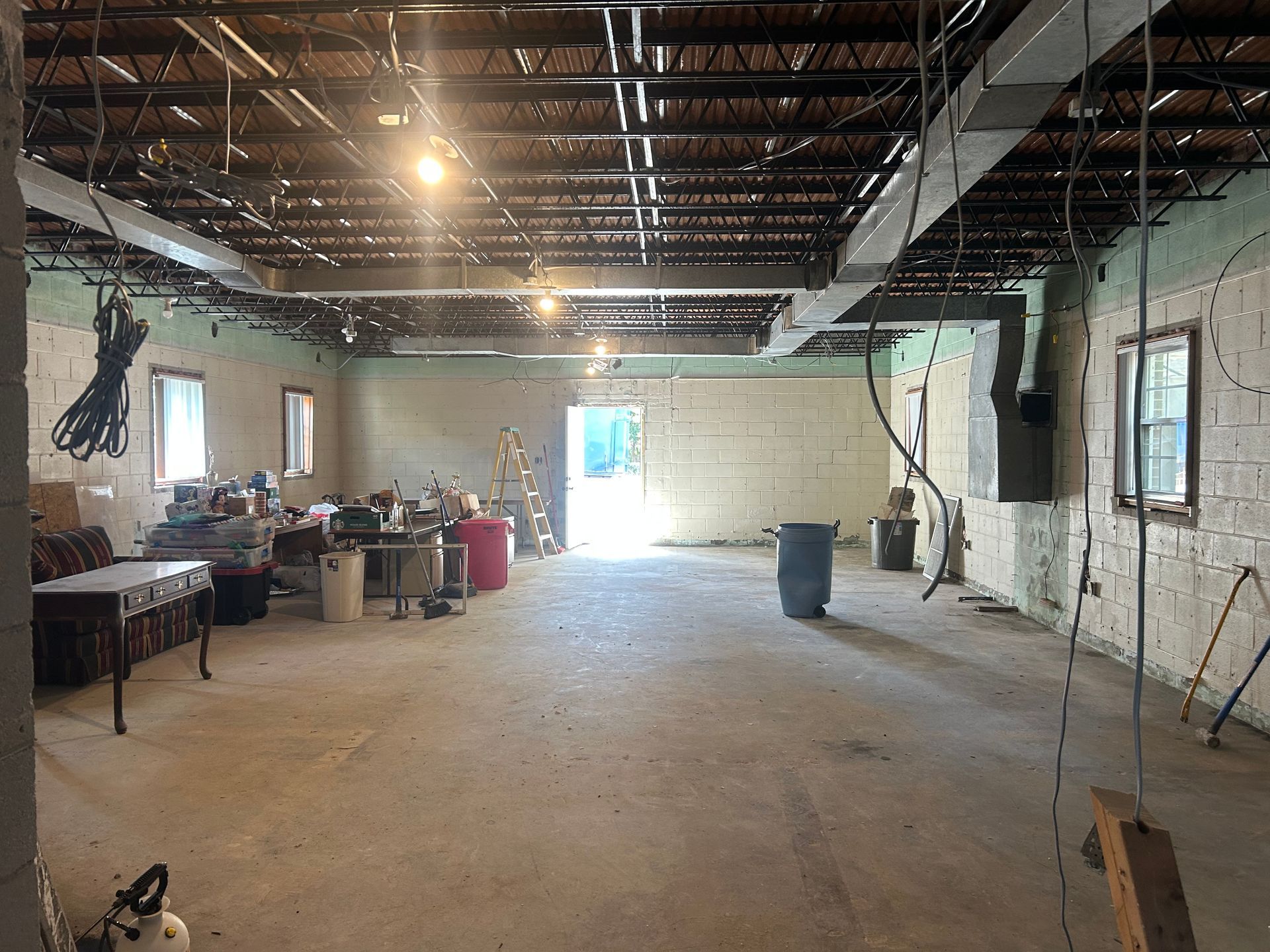 Interior of a room under construction, with exposed ceiling beams, unfinished walls, and a door to outside.