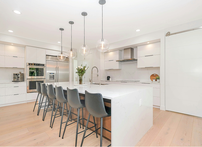 Modern white kitchen with island seating and pendant lights.