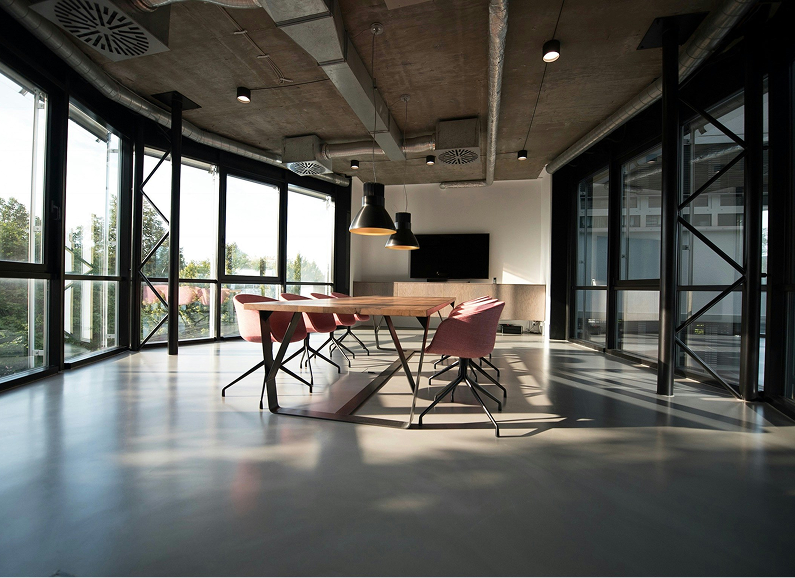 Meeting room with large windows, wooden table, pink chairs, and black pendant lights.