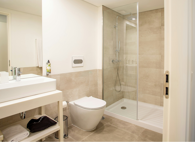 Modern bathroom with wooden vanity, black sinks/fixtures, toilet, and light stone tile walls.