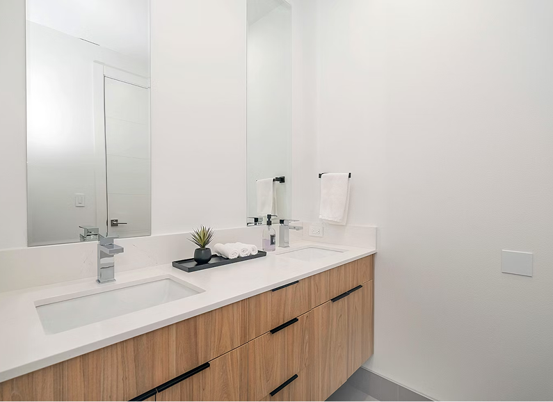 Modern bathroom with wood vanity, black fixtures, round mirror, and textured light-colored tile walls.