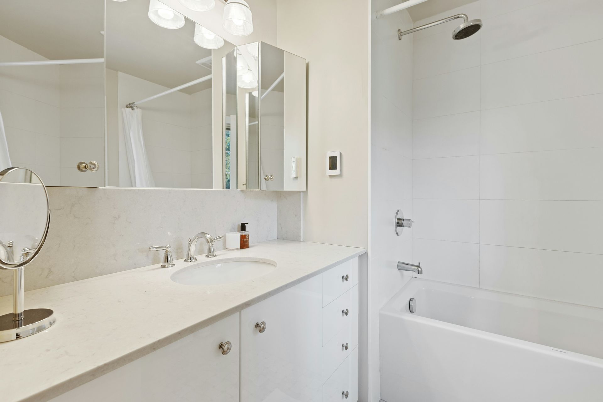 White bathroom with a vanity, mirror, and a shower/tub combo.