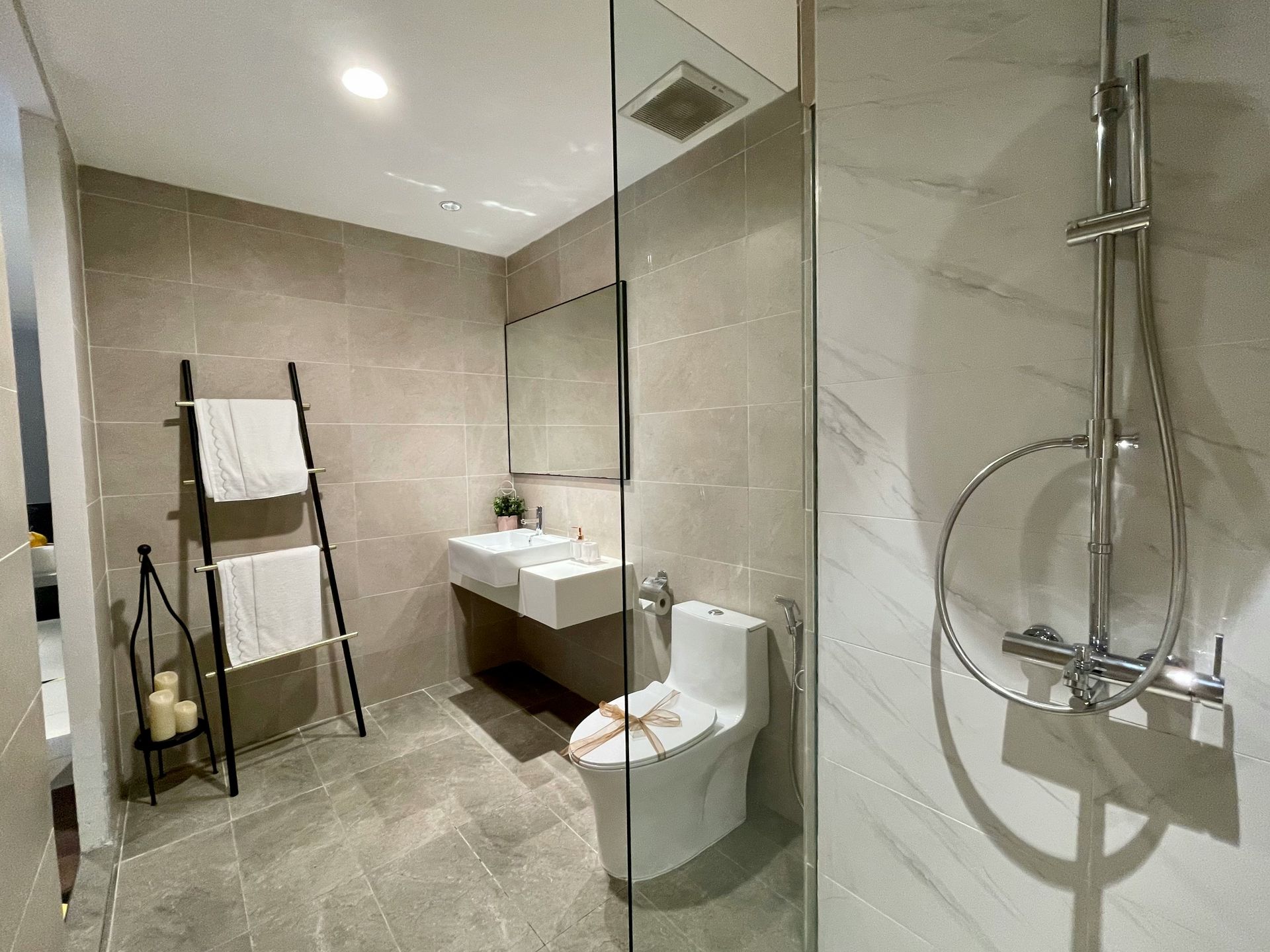 Modern bathroom with shower, toilet, sink, and towel rack. Neutral colors, tiled walls, and a glass shower door.