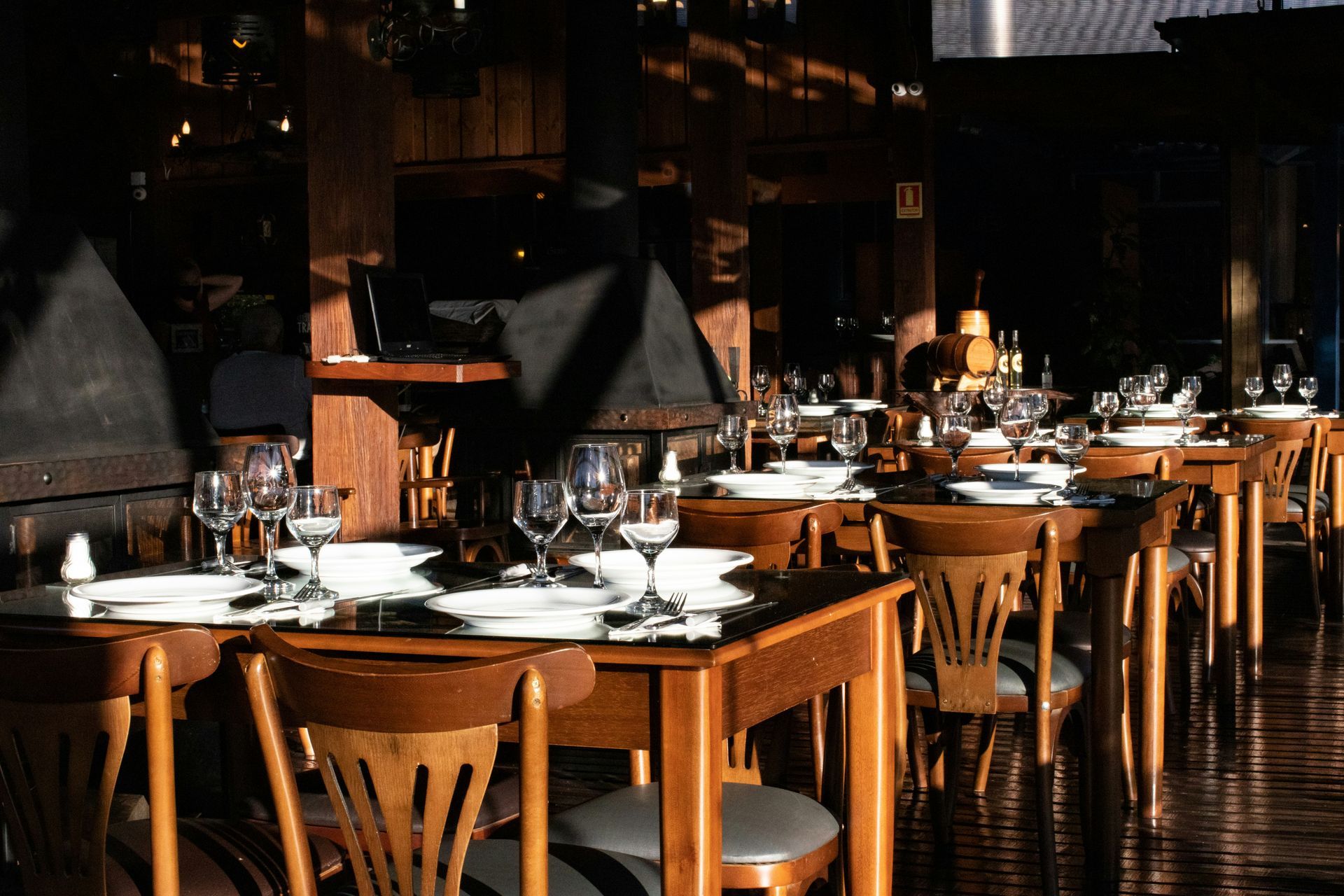 Restaurant interior with wooden tables set for diners. Sunlight streams across the tables and chairs.