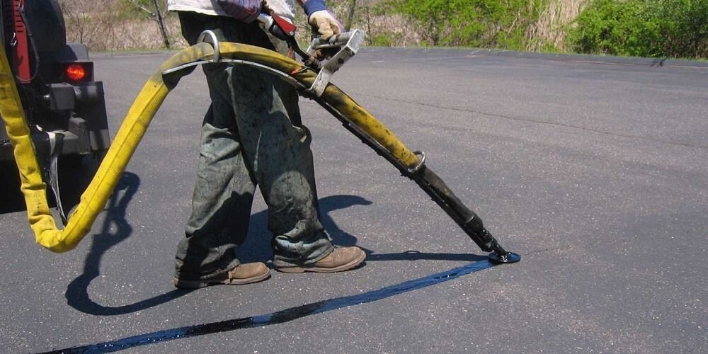 A man is standing on a road holding a yellow hose.