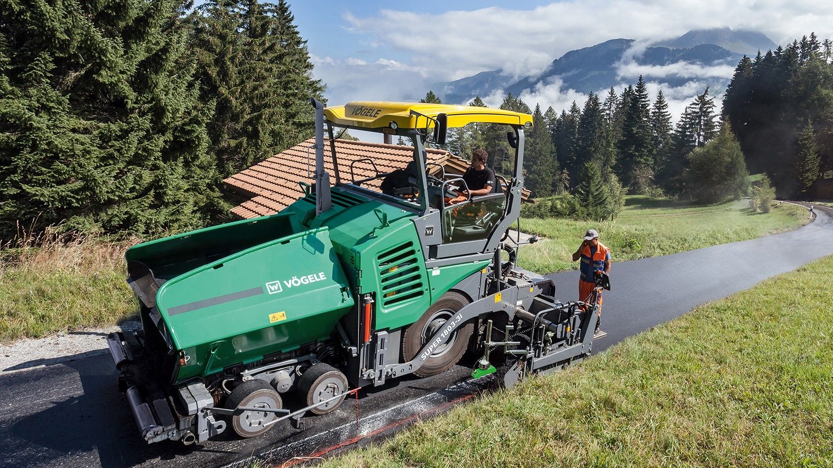 A man is standing next to a green machine that is laying asphalt on a road.