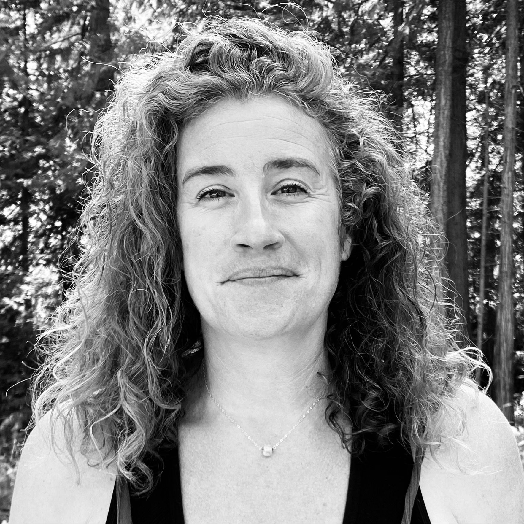 a black and white photo of Lyndsay Fluharty smiling in front of some trees.