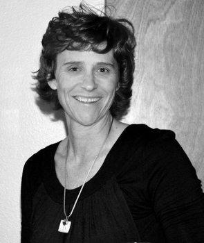 KELLI PARCHER wearing a black shirt and a necklace is smiling in a black and white photo .