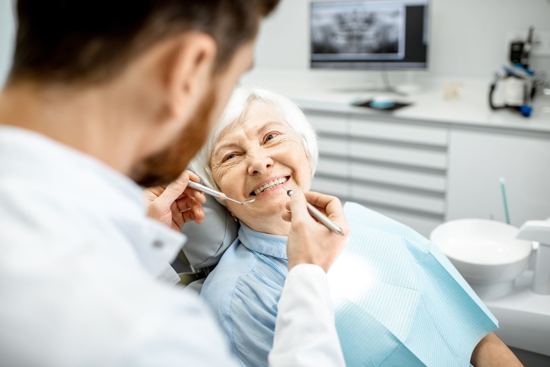 An Elderly Woman Is Sitting in A Dental Chair While a Dentist Examines Her Teeth.