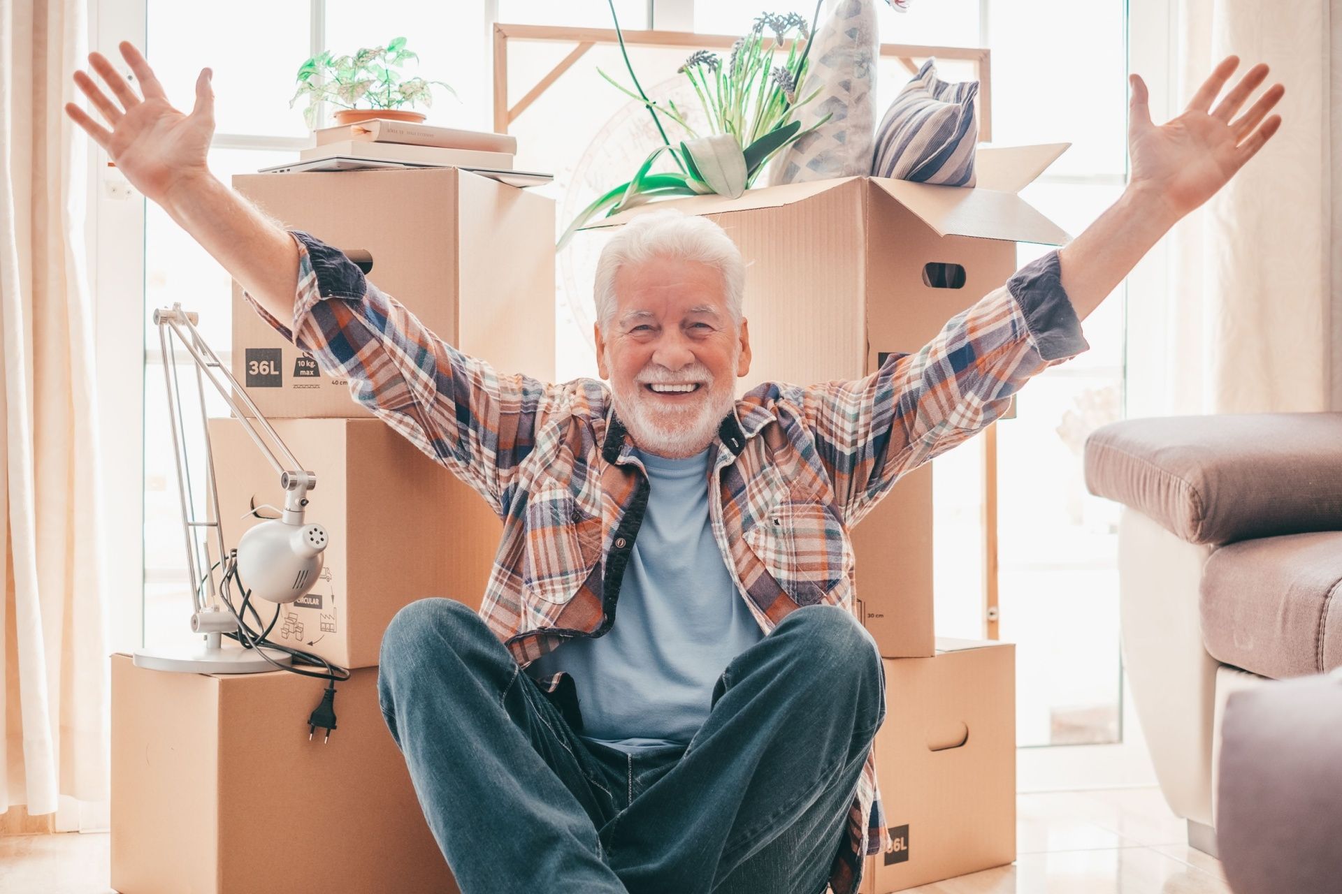 An elderly man is sitting on the floor in front of a pile of cardboard boxes.