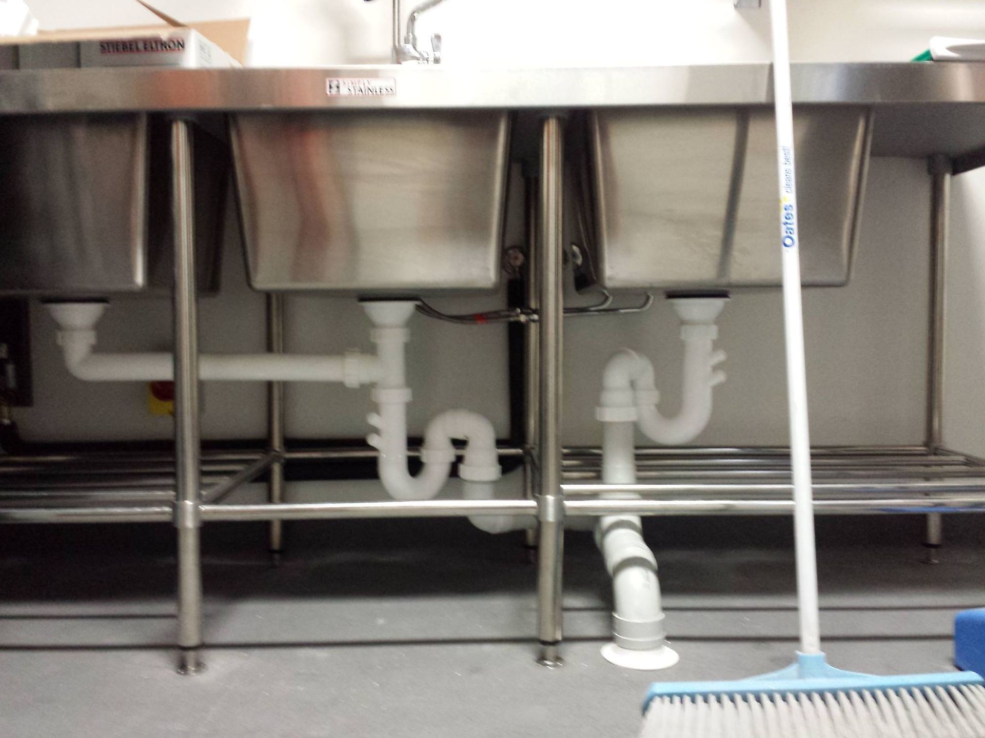 A stainless steel sink with a broom underneath it