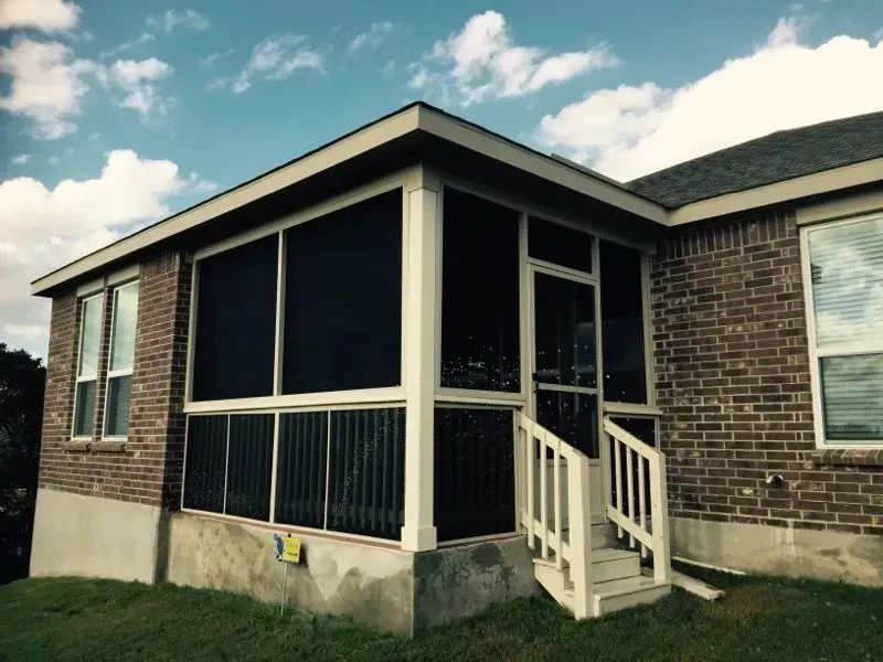 A screened in porch on the side of a brick house.