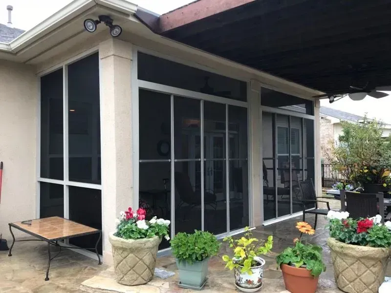 A screened in porch with potted plants and a table.