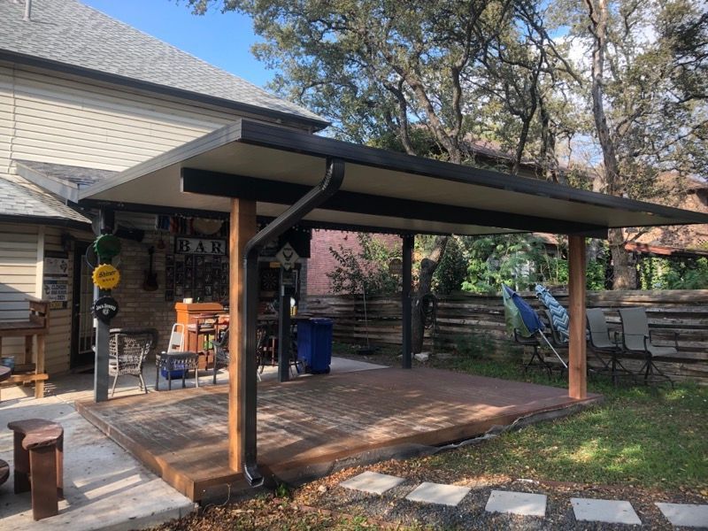 A patio with a roof and a wooden deck in the backyard of a house.