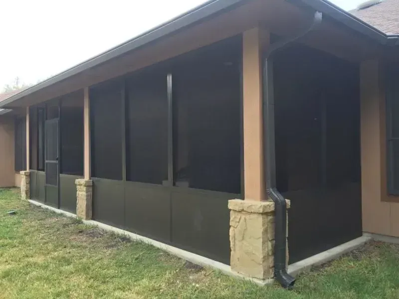 A screened in porch with black screens on the side of a house.