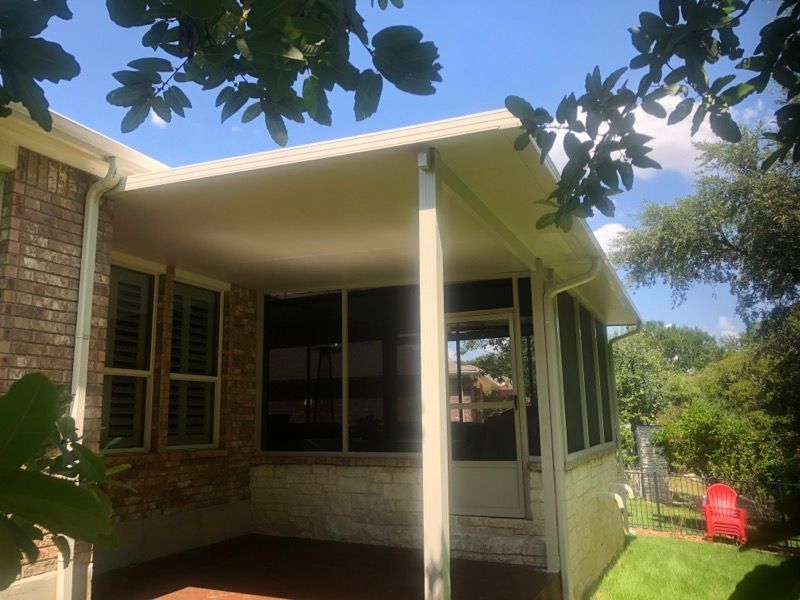 A screened in porch with a brick house in the background.