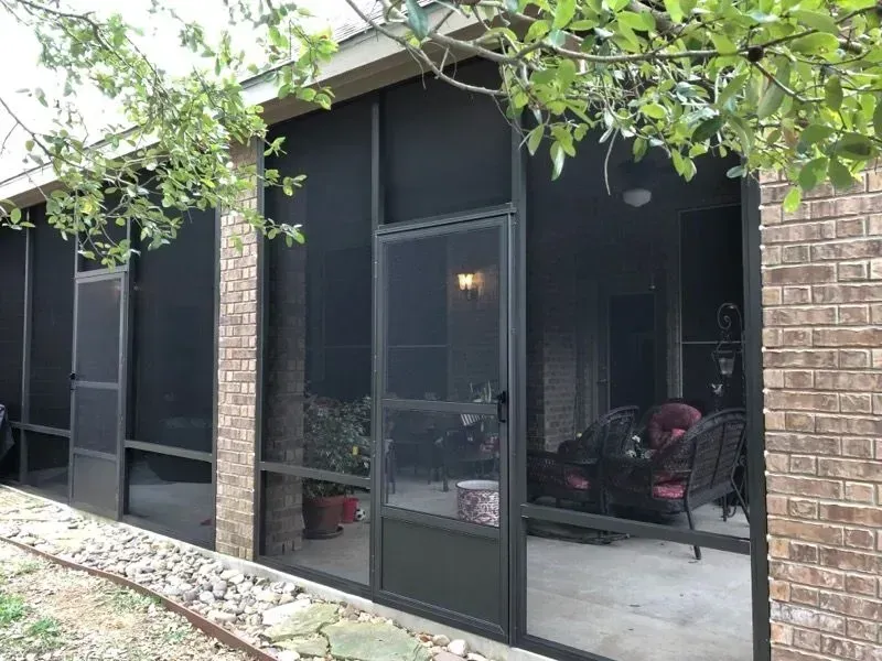 A screened in porch with a brick wall and sliding glass doors.