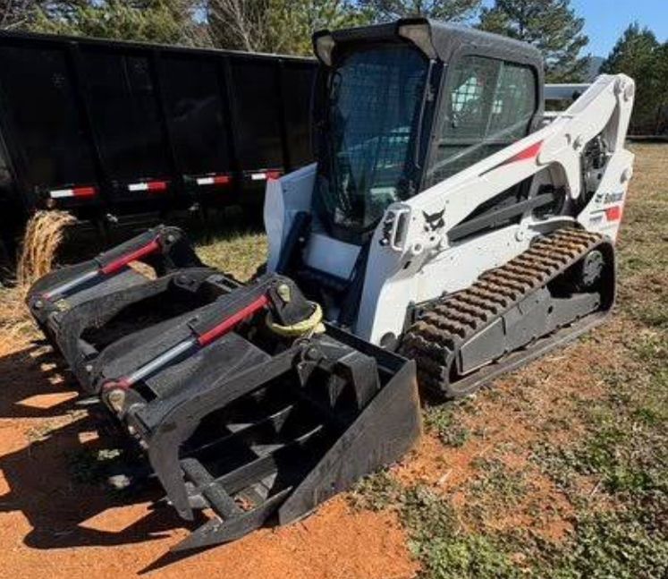 Crane lifting a large tree over a house with a brown roof on a sunny day.