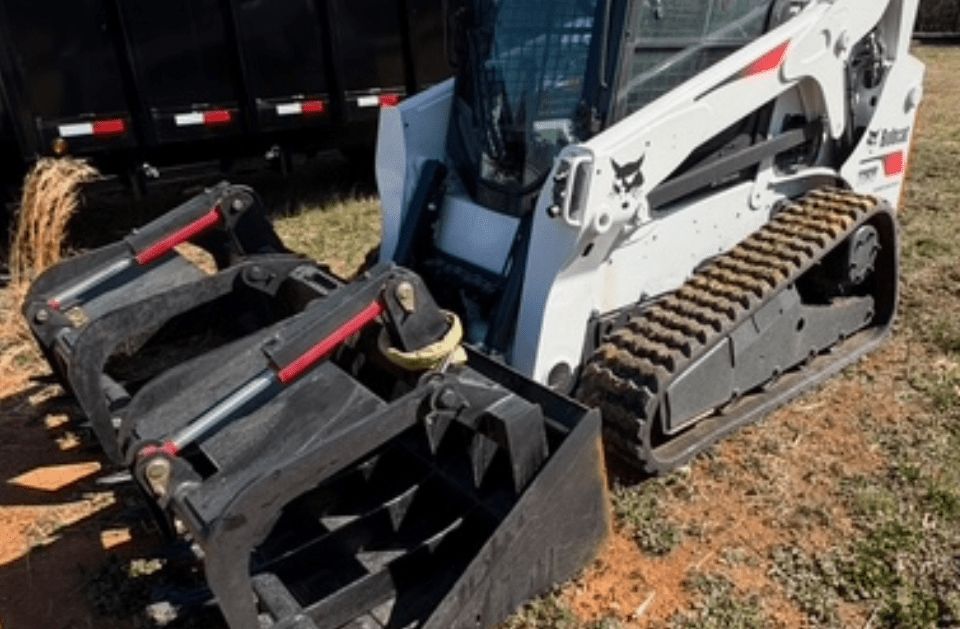 Bobcat compact track loader with grapple bucket on a dirt surface.