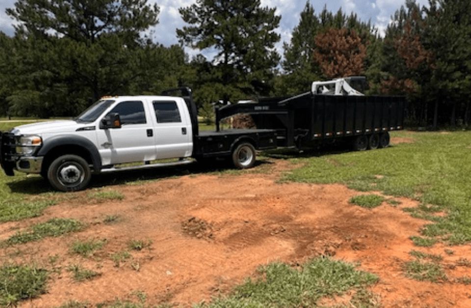 White pickup truck towing a black trailer on a grassy area, trees in the background.