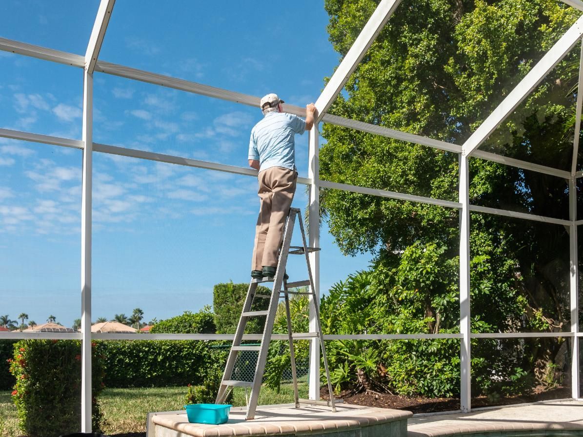 A man is standing on a ladder working on a pool enclosure.