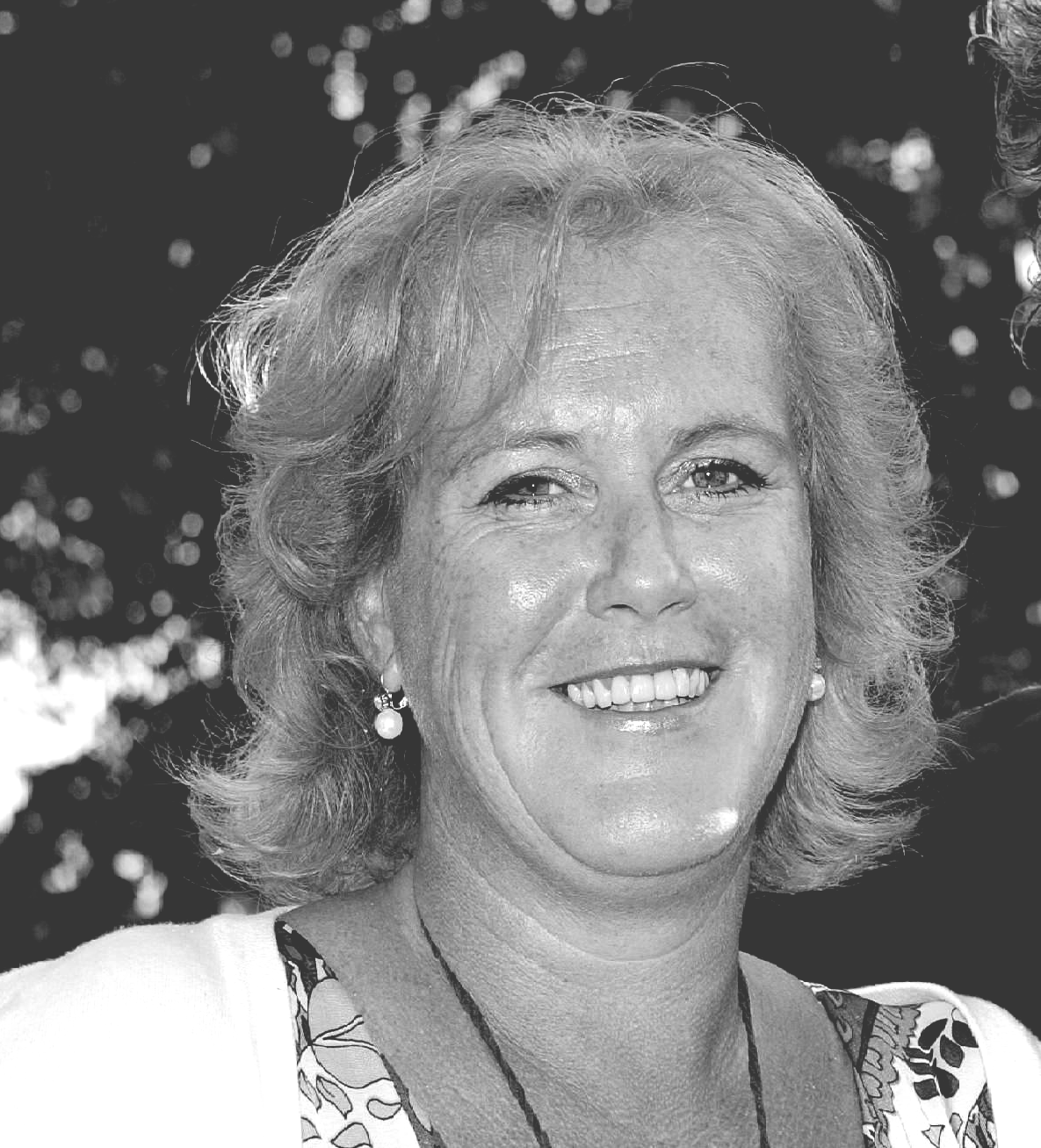 Lachende vrouw met blond haar, pareloorbellen en een top met print.