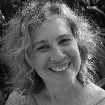 Een vrouw met krullend haar lacht buiten.