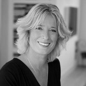 Blonde vrouw lacht naar de camera. Ze draagt een zwart topje, een ketting en oorringen.