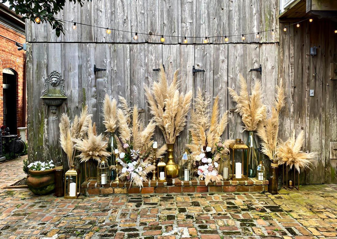 A row of pampas grass in vases in front of a wooden wall.
