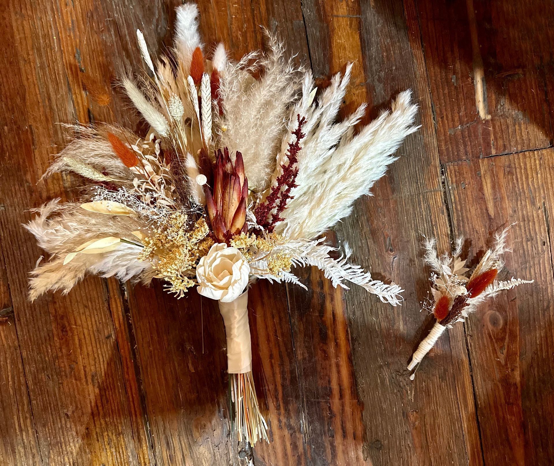 A bouquet of dried flowers and a boutonniere are sitting on a wooden floor.