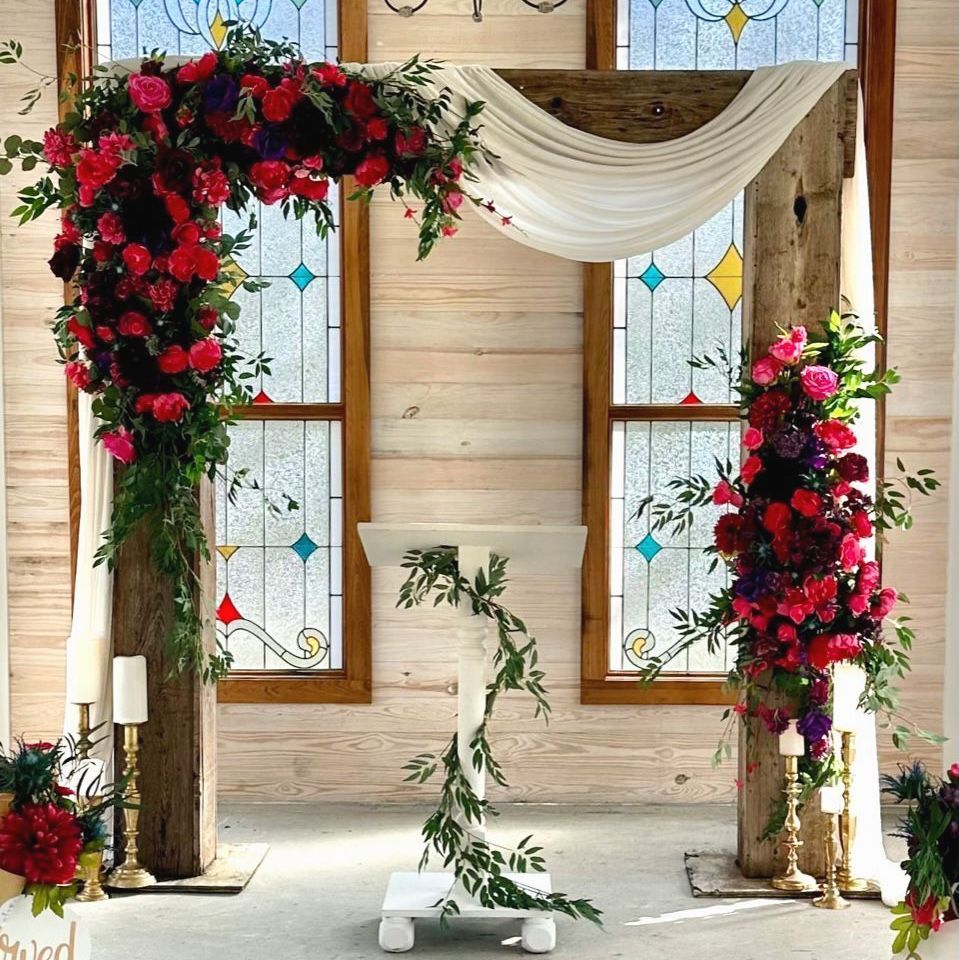 A wedding arch with flowers and candles in front of stained glass windows