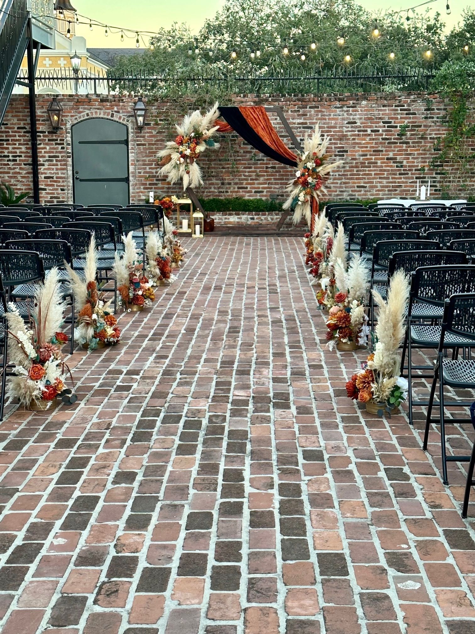 A brick walkway lined with chairs and flowers for a wedding ceremony.