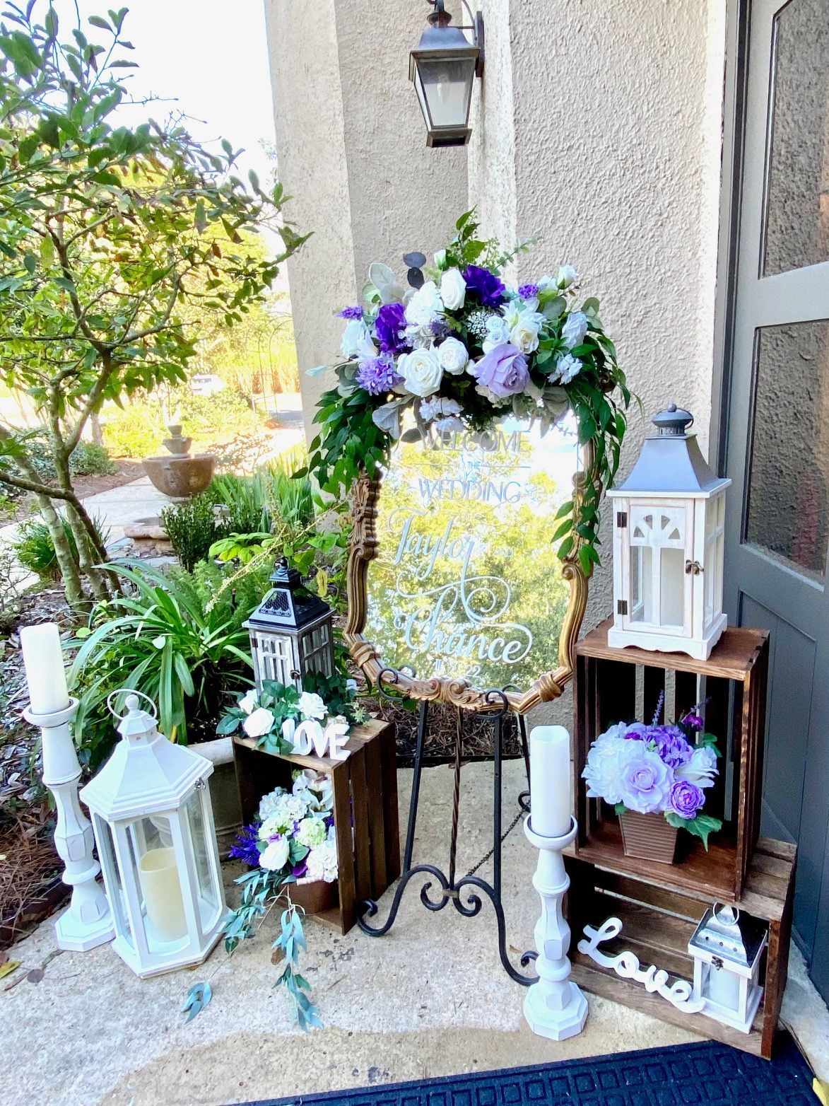 A mirror is surrounded by flowers and lanterns on a porch.