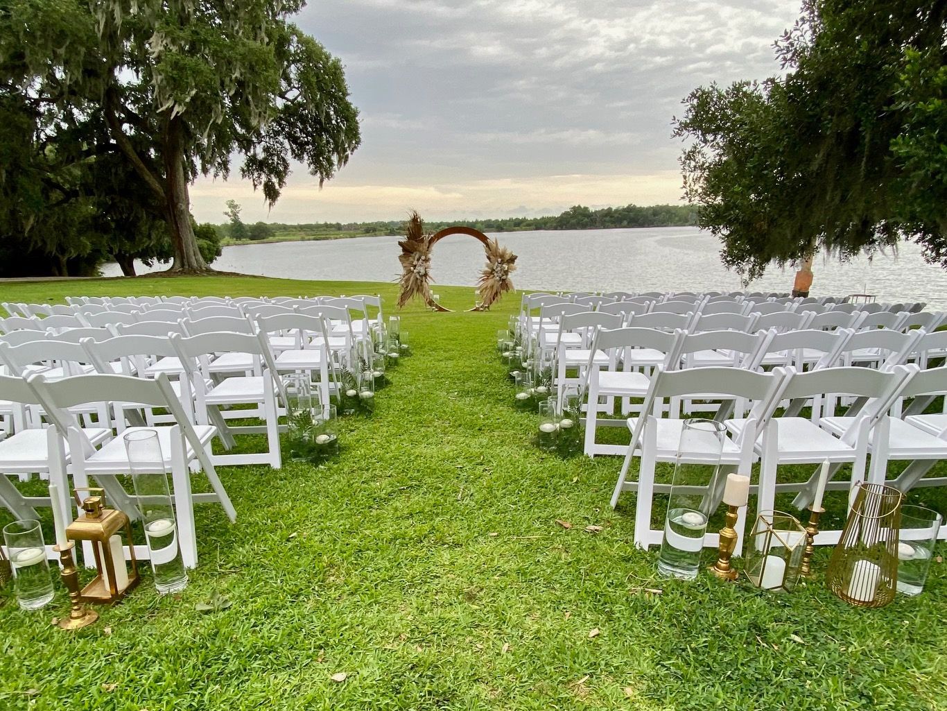 A row of white chairs sitting on top of a lush green field next to a body of water.