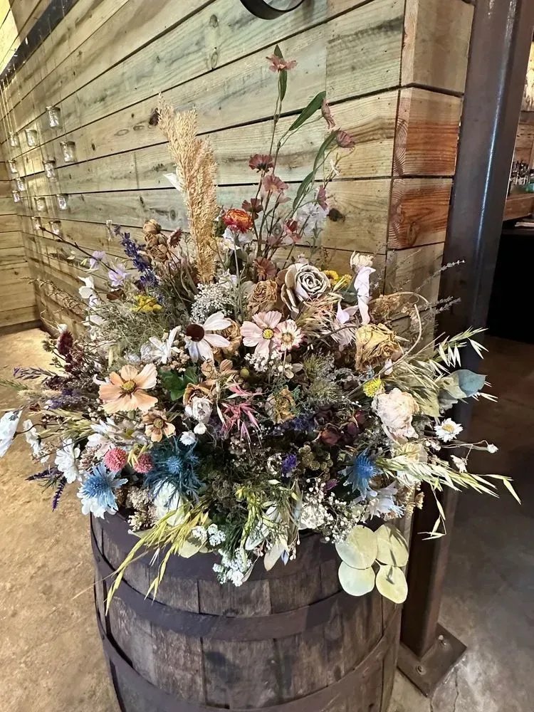 A wooden barrel filled with flowers is sitting in front of a wooden wall.