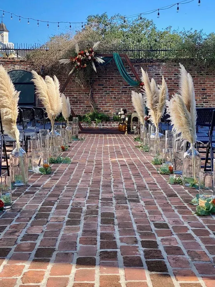 A brick walkway lined with pampas grass and candles for a wedding ceremony.