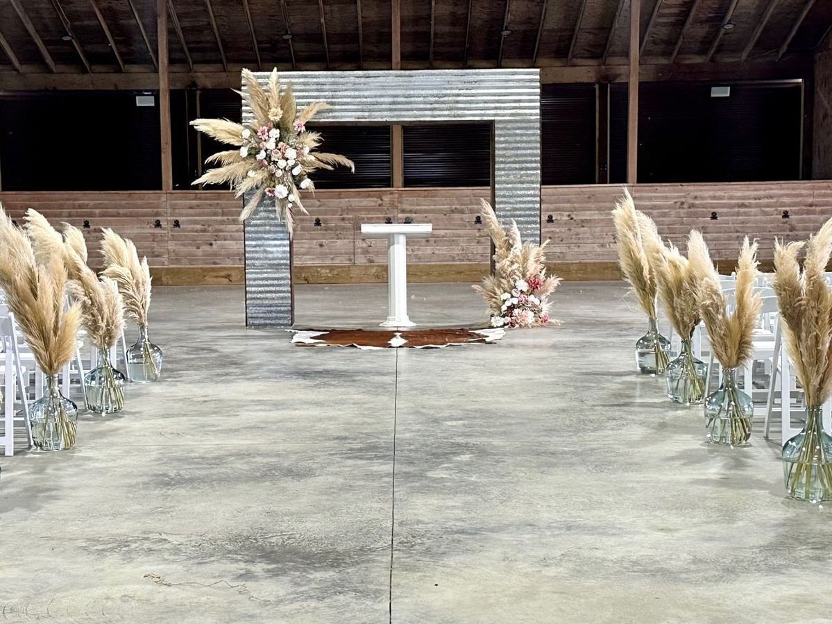 A row of chairs are lined up in front of a altar decorated with pampas grass and flowers.