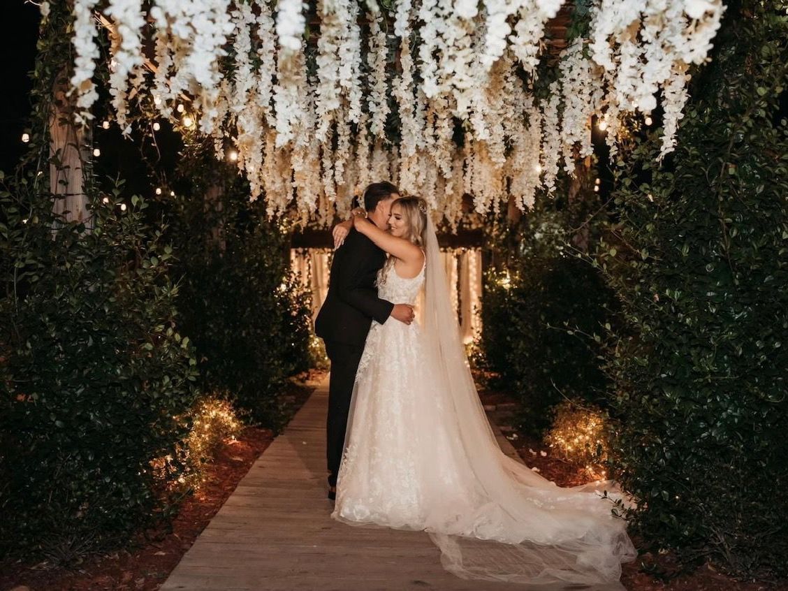 A bride and groom are kissing under a chandelier of white flowers.