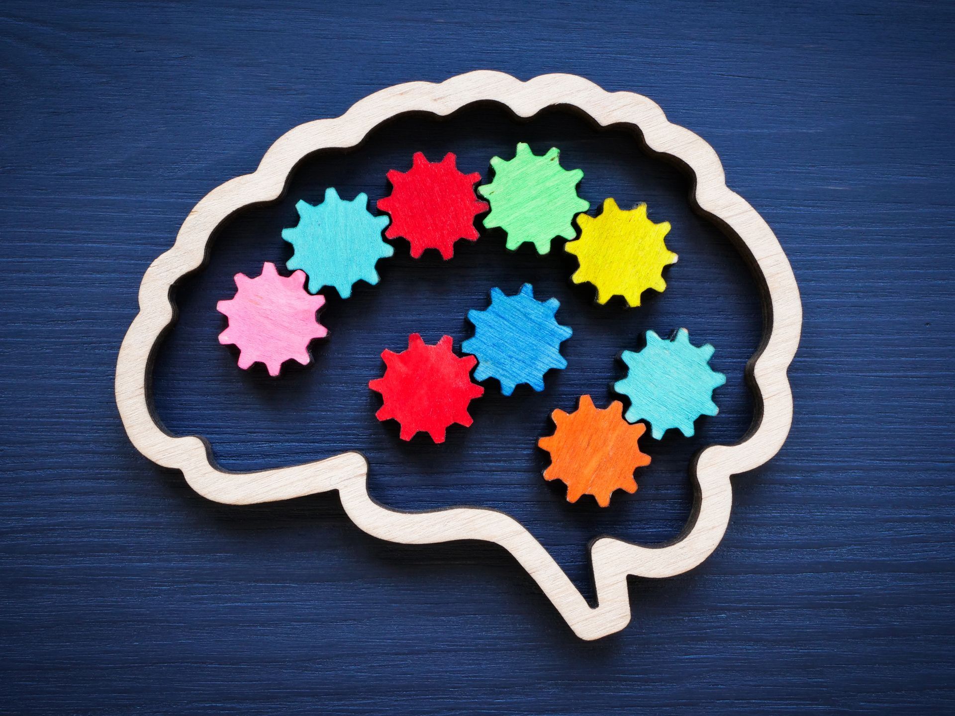 Esquema de cerebro de madera lleno de formas de engranajes de colores sobre un fondo azul.