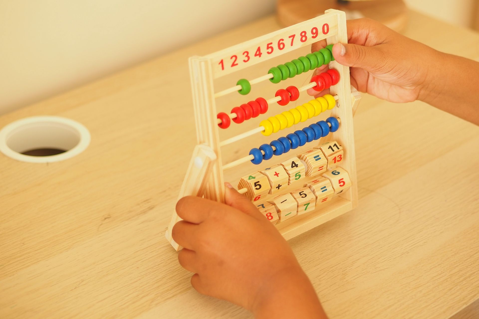 Niño sosteniendo un ábaco de madera con cuentas de colores sobre un escritorio de color claro.