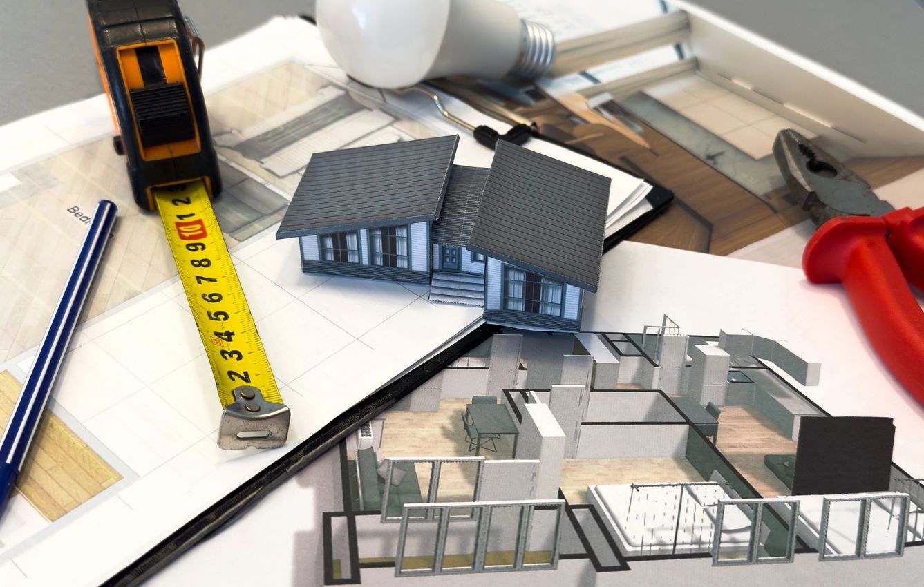 Modellino architettonico con metro a nastro, righello e martello rosso su un tavolo da lavoro.