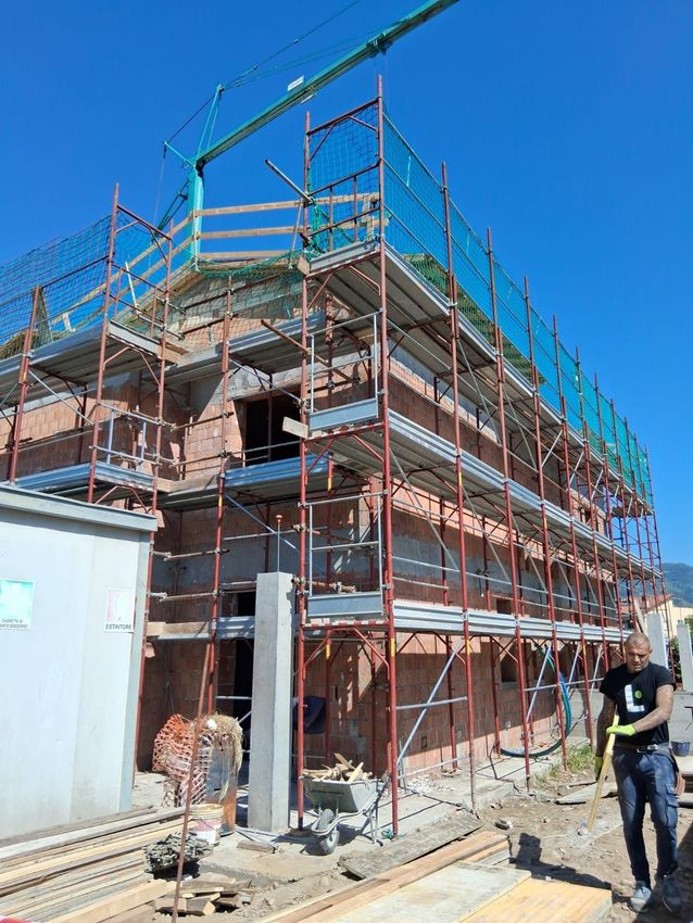 Stanza interna non rifinita con pareti grezze, soffitto in cemento, materiali edili e attrezzi sparsi sul pavimento.