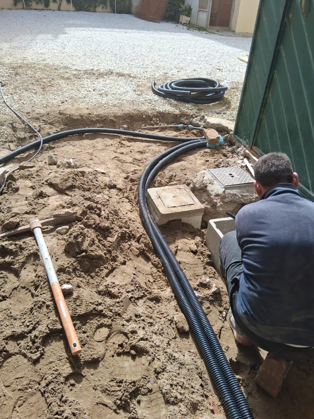 Operaio inginocchiato accanto a tubi di drenaggio neri e a una trincea di ghiaia in un cortile