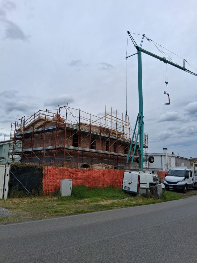 Cantiere edile con alte gru e un moderno edificio parzialmente costruito sotto un cielo azzurro brillante.