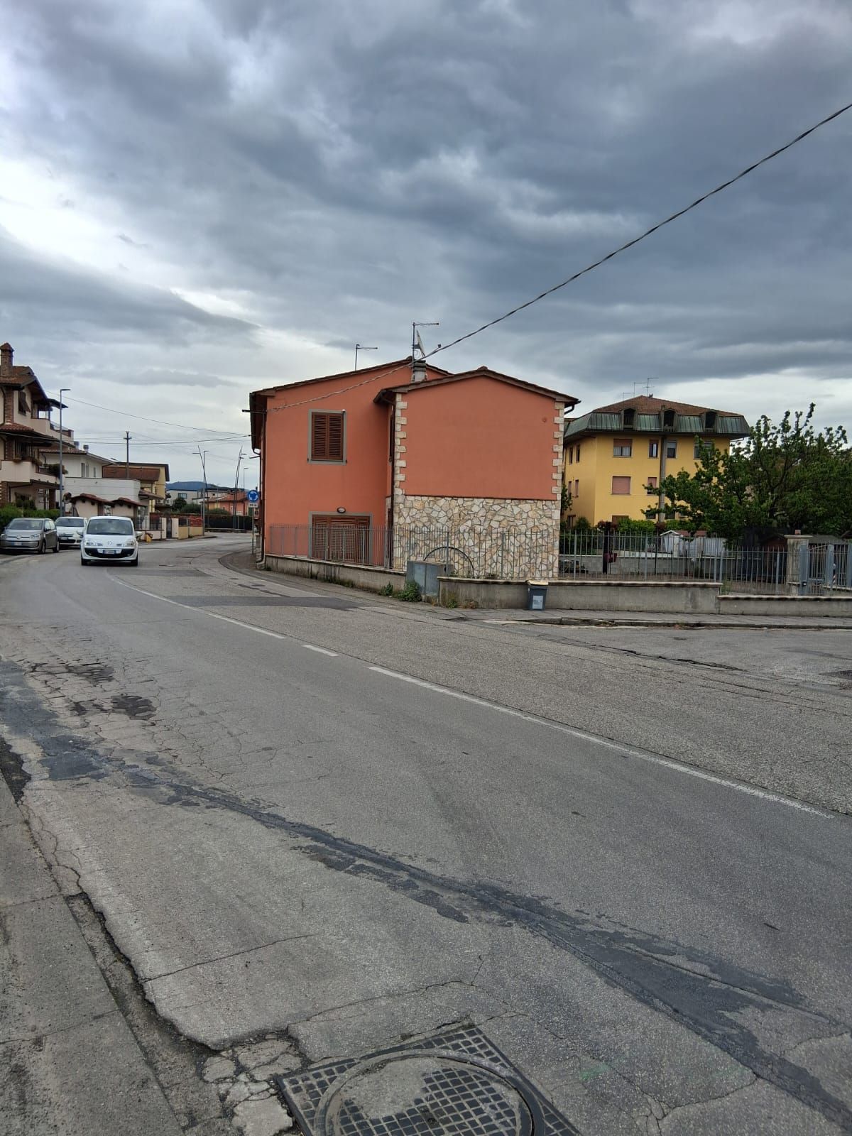 Una strada tranquilla con case arancioni e gialle sotto un cielo nuvoloso, vista da una strada dissestata.
