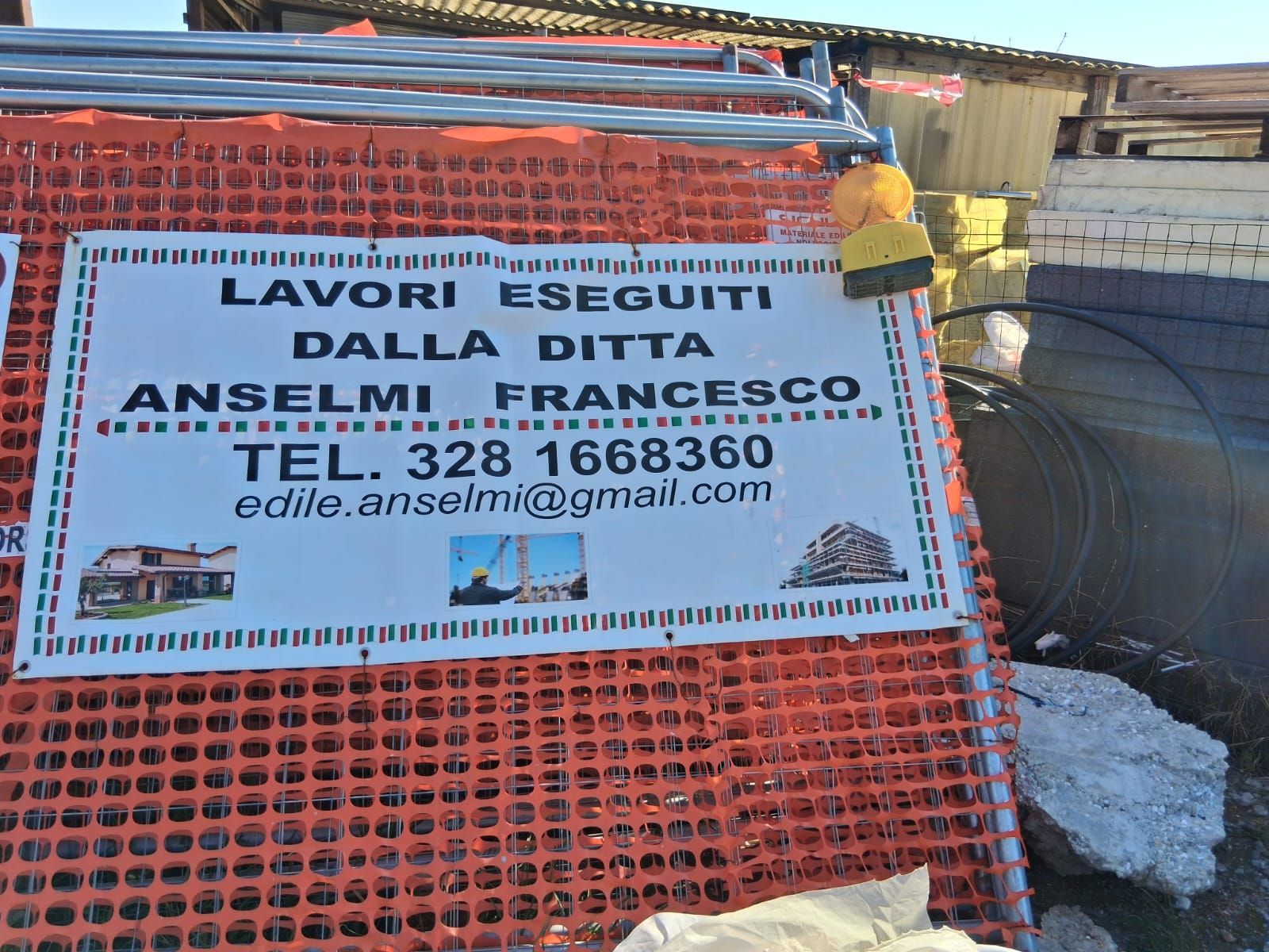 Construction sign on orange mesh fence reading “Lavori eseguiti da Ditta Anselmi Francesco”
