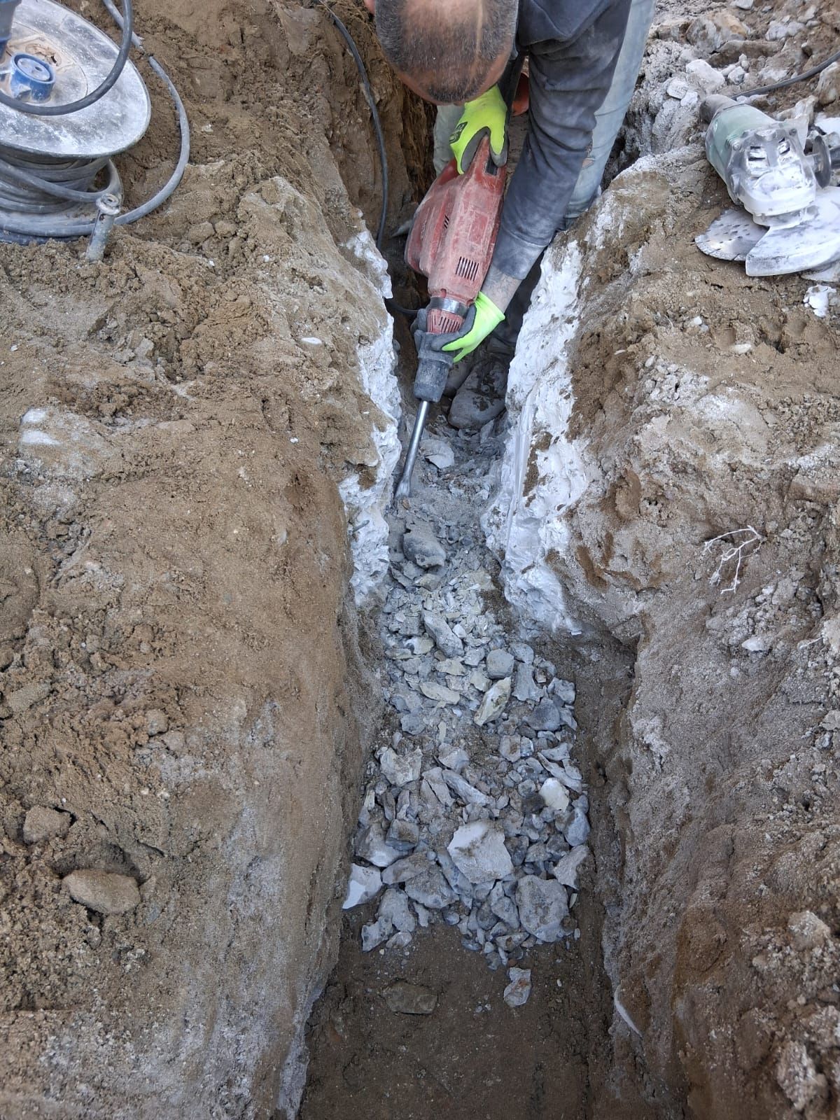 Un operaio utilizza un utensile elettrico in una stretta trincea di terra piena di macerie e detriti simili a ghiaccio.