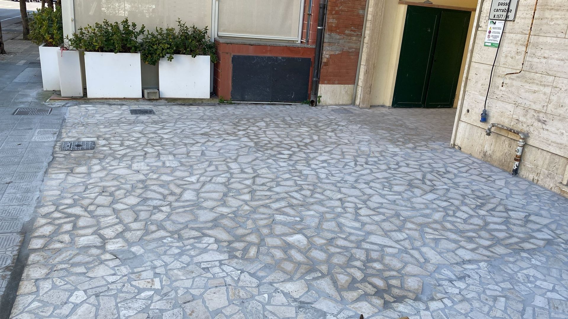 Cortile lastricato con fioriere bianche e l'ingresso di un edificio sullo sfondo.
