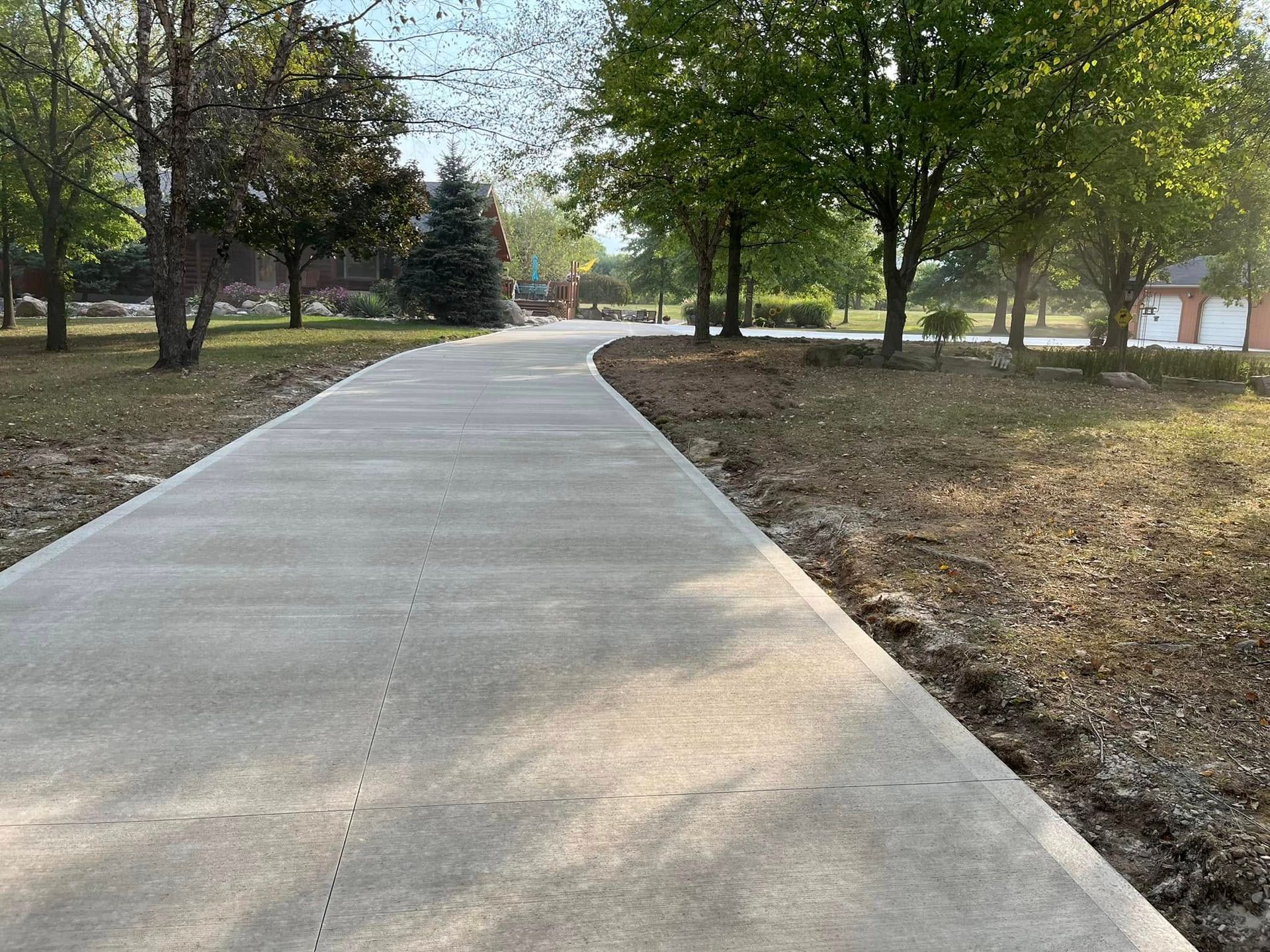 Concrete path curving through a park with trees and grass.